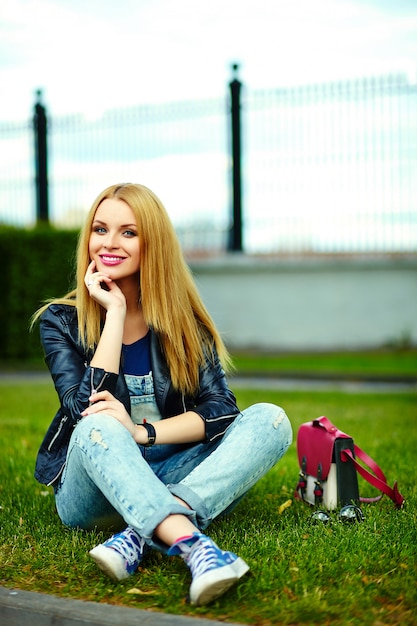 portret van schattige grappige blonde moderne sexy stedelijke jonge stijlvolle lachende vrouw meisje model in heldere moderne doek buiten zitten in het park in jeans met roze tas
