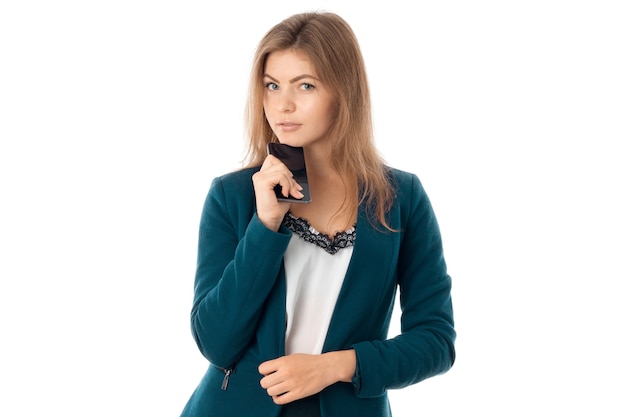 Portret van serieuze jonge zakenvrouw in blauwe jas met mobiele telefoon in de hand kijkend naar de camera geïsoleerd op een witte achtergrond