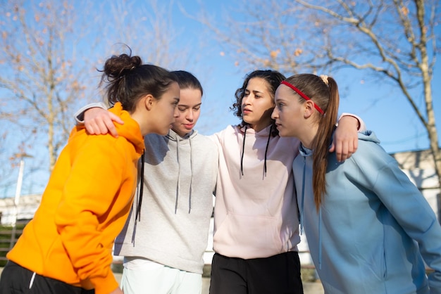 Portret van serieuze meisjes die zich voorbereiden om een voetbalwedstrijd te beginnen. Voetbalteam van vier meisjes die op het veld staan en hun schouders knuffelen en de spelstrategie bespreken. Gezonde levensstijl en teamsportconcept