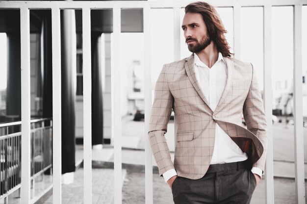 portret van sexy knappe mode mannelijk model man gekleed in elegante beige geruit pak die zich voordeed op de straat achtergrond