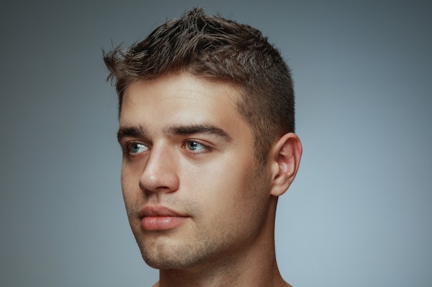 Portret van shirtless jongeman geïsoleerd op grijze studio achtergrond. kaukasisch gezond mannelijk model kant kijken en poseren. concept van de gezondheid en schoonheid van mannen, zelfzorg, lichaams- en huidverzorging.