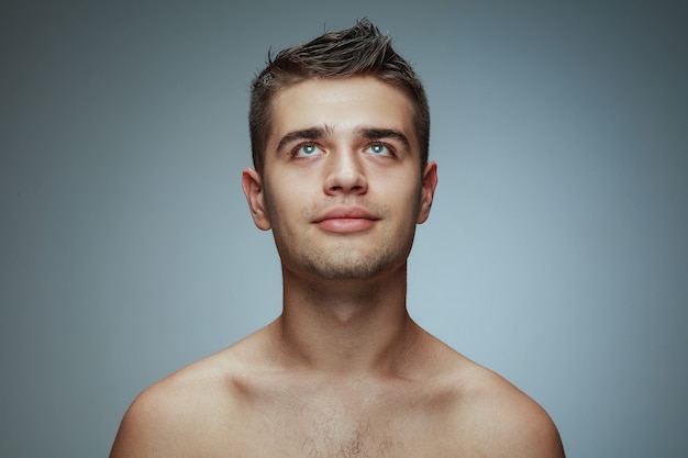 Portret van shirtless jongeman geïsoleerd op grijze studio achtergrond. Kaukasisch gezond mannelijk model opzoeken en poseren. Concept van de gezondheid en schoonheid van mannen, zelfzorg, lichaams- en huidverzorging.