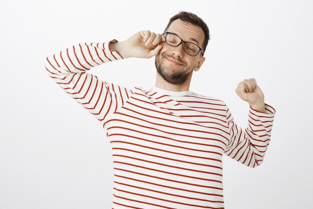 Portret van slaperig moe blij man in glazen, oog wrijven en breed glimlachen terwijl die zich uitstrekt van uitputting, willen slapen na een lange werkdag