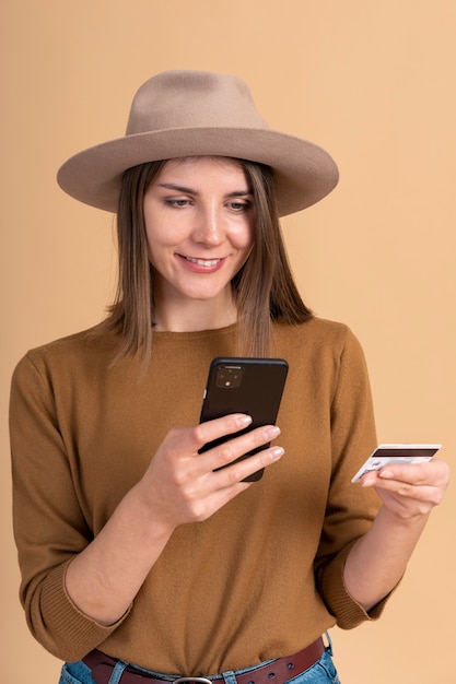 Portret van smileyvrouw met hoed die reiskaartjes boekt met smartphone en creditcard