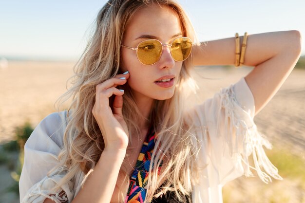 Portret van speels glimlachend blond meisje dat met haren speelt, plezier heeft en geniet van de zomer op het strand.