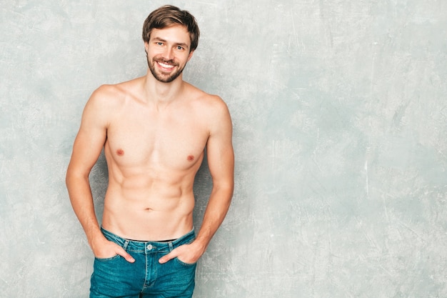 Portret van sportieve knappe sterke man. Gezond lachend atletisch fitnessmodel poseren in de buurt van grijze muur in spijkerbroek.