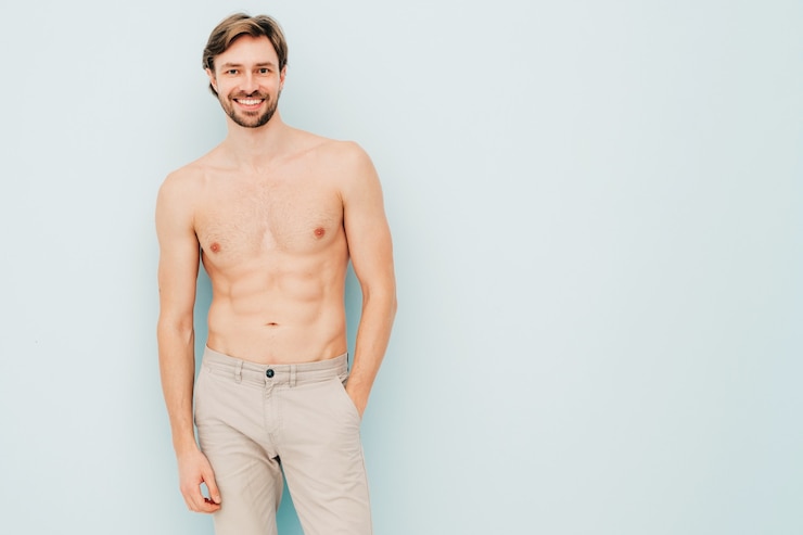Gratis Foto portret van sportieve knappe sterke man. gezond lachend atletisch fitnessmodel poseren in de buurt van lichtblauwe muur