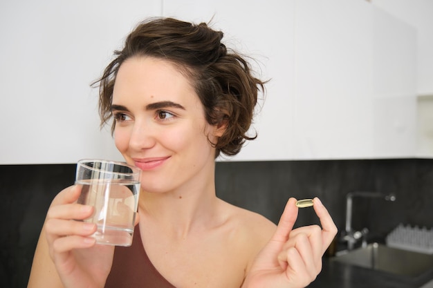 Portret van sportvrouw drinkwater dat vitaminen voedingssupplementen neemt voor een gezonde huid met om