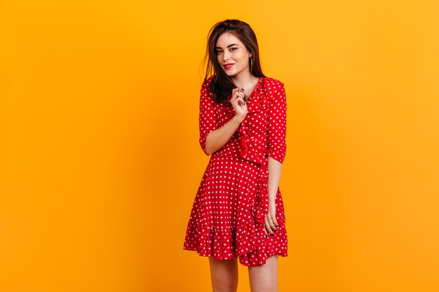 Portret van stijlvol jong meisje in een rode jurk. Model is schattig lachend op oranje muur.