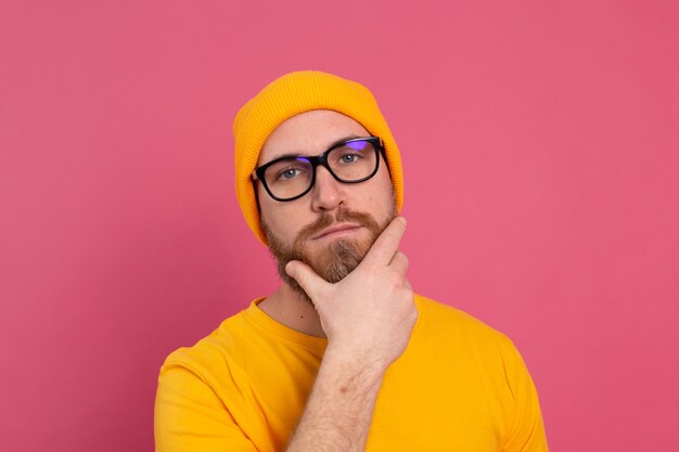 Portret van stijlvolle knappe Europese bebaarde man in casual geel overhemd hoed en bril op roze achtergrond