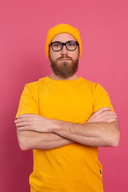Portret van stijlvolle knappe Europese bebaarde man in casual geel overhemd hoed en bril op roze achtergrond