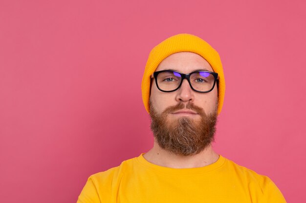 Portret van stijlvolle knappe Europese bebaarde man in casual gele overhemdshoed en bril op roze