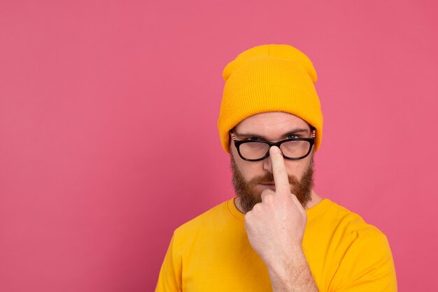 Portret van stijlvolle knappe Europese bebaarde man in casual gele overhemdshoed en bril op roze