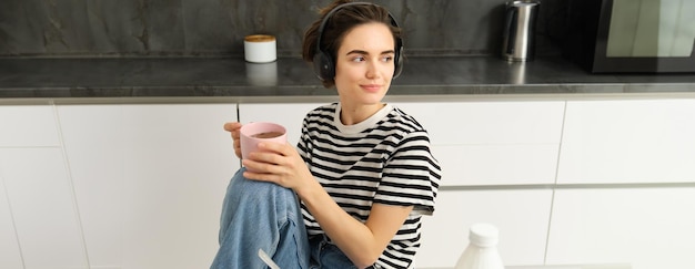 Portret van stijlvolle moderne vrouw in koptelefoon luistert naar muziek en drinkt thee eet granen met melk