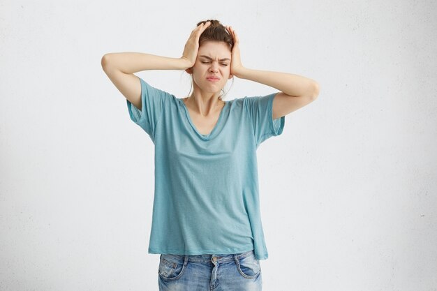 Portret van stressvolle blonde vrouw in vrijetijdskleding met hoofdpijn hand in hand op haar hoofd fronsen haar gezicht met ontevreden blik.