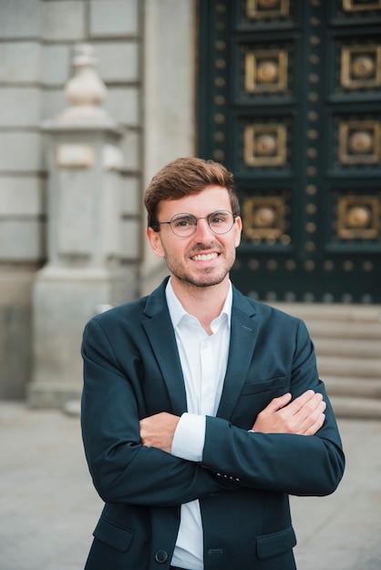 Portret van succesvolle jonge zakenman met zijn gekruiste wapens het bekijken camera