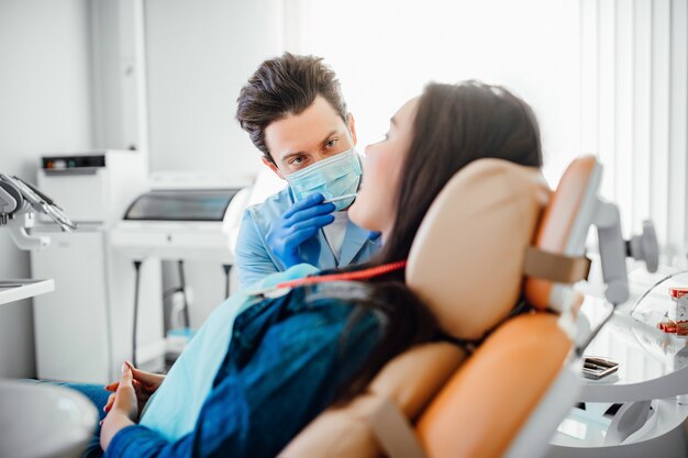 Portret van tandarts in blauw masker die met patiënt in moderne kliniek werkt.