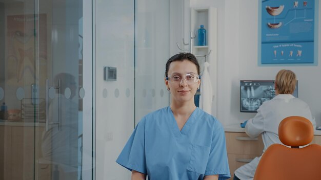 Portret van tandheelkunde verpleegkundige met uniforme en beschermende bril in stomatologie kabinet. Zelfverzekerde assistent die zich voorbereidt op mondzorgonderzoek, tandartspraktijk doet. Vrouw kijkt naar de camera