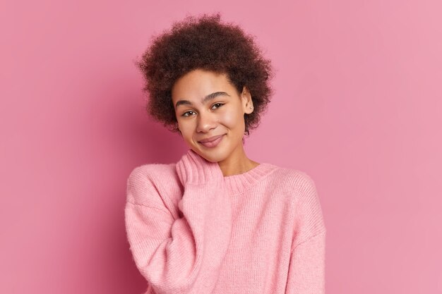 Portret van tevreden duizendjarige vrouw houdt hand op nek ziet er zachtjes uit en draagt een casual trui