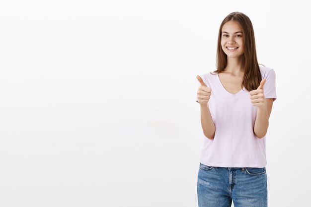 Portret van tevreden gelukkig en tevreden goed uitziende vriendelijke vrouw in casual blouse en spijkerbroek duimen opdagen en breed glimlachend tevreden met de goede kwaliteit van het product