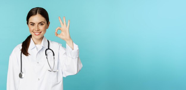 Portret van tevreden glimlachende medische werker vrouw arts die oke ok nul geen probleemgebaar toont uitstekend teken dat tevreden over torquoise achtergrond staat