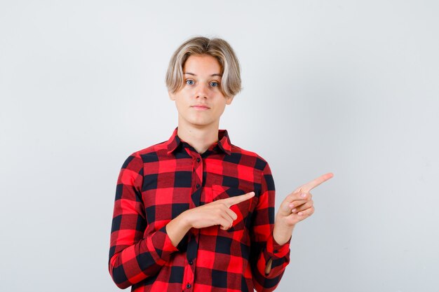 Portret van tiener blond mannetje wijzend naar de rechterbovenhoek in casual shirt en peinzend vooraanzicht