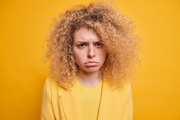 Portret van trieste ongelukkige jonge europese vrouw met natuurlijk krullend haar mokken van iets oneerlijks wordt beledigd portemonnees lippen drukt negatieve emoties uit heeft een droevige teleurgestelde uitdrukking.