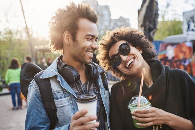 Portret van twee geliefden met afro-kapsels, wandelen in het park en koffie drinken terwijl ze praten en genieten van tijd doorbrengen op food festival.