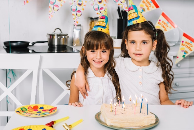 Portret van twee glimlachende meisjes met feestmutsen op hoofd die zich achter de verjaardagscake bevinden