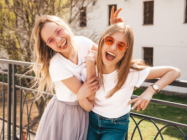 Portret van twee jonge mooie blonde glimlachende hipster meisjes in kleren van de trendy de zomer witte t-shirt. . positieve modellen hebben plezier in een zonnebril