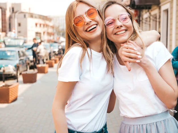 Gratis foto portret van twee jonge mooie blonde glimlachende hipster meisjes in kleren van de trendy de zomer witte t-shirt. . positieve modellen hebben plezier in een zonnebril