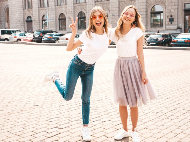 Portret van twee jonge mooie blonde glimlachende hipster meisjes in kleren van de trendy de zomer witte t-shirt.