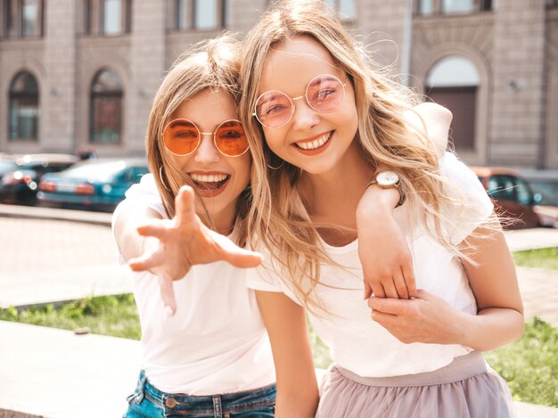 Portret van twee jonge mooie blonde glimlachende hipster meisjes in kleren van de trendy de zomer witte t-shirt.