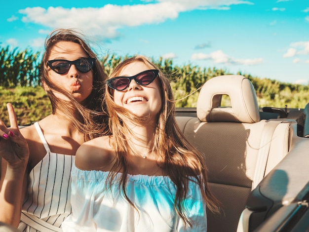 Portret van twee jonge mooie en glimlachende hipstermeisjes in convertibele auto