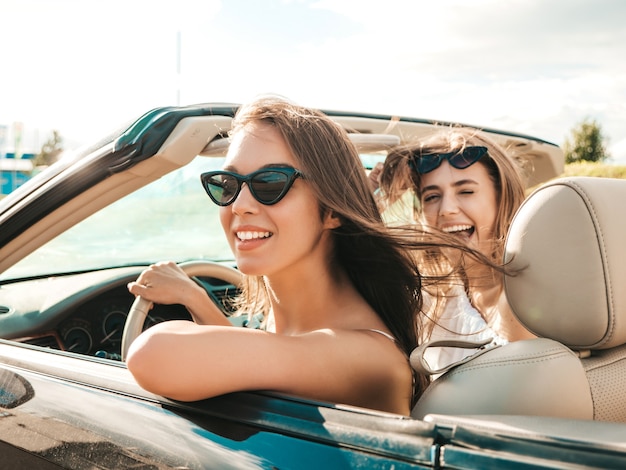 Portret van twee jonge mooie en glimlachende hipstervrouwen in convertibele auto