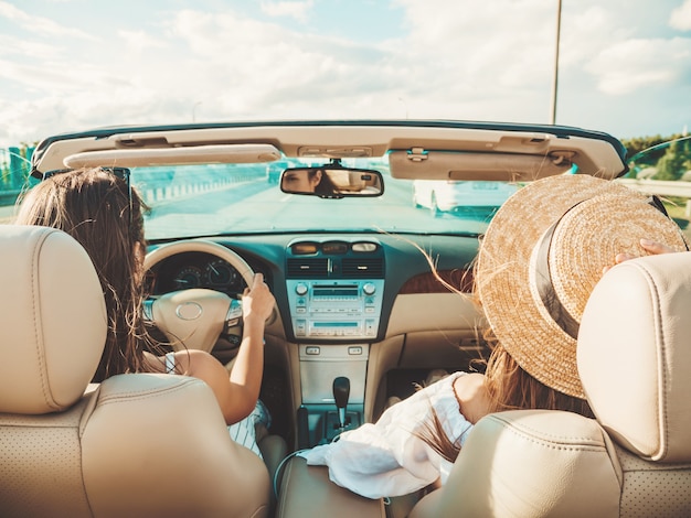 Portret van twee jonge mooie en glimlachende hipstervrouwen in convertibele auto