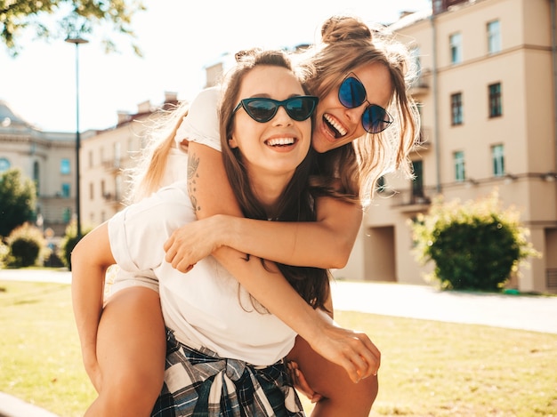 Portret van twee jonge mooie glimlachende hipstermeisjes in trendy zomerse witte t-shirtkleren