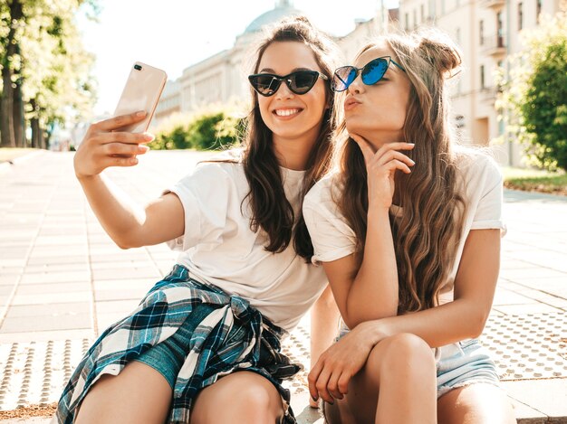 Portret van twee jonge mooie glimlachende hipstervrouwen in trendy zomerse witte t-shirtkleren