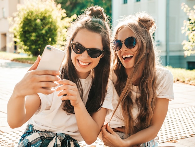 Portret van twee jonge mooie glimlachende hipstervrouwen in trendy zomerse witte t-shirtkleren