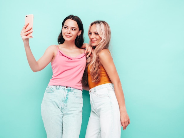 Portret van twee jonge mooie lachende brunette hipster vrouw in trendy zomerkleren Sexy zorgeloze vrouwen poseren in de buurt van blauwe muur Positieve modellen plezier vrolijk en gelukkig nemen selfie