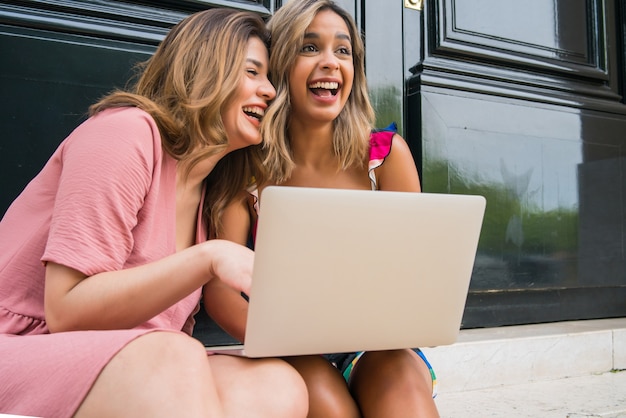 Portret van twee jonge vrienden die een laptop gebruiken terwijl ze buiten zitten. Stedelijk begrip. Technologieconcept.