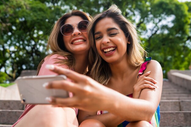 Portret van twee jonge vrienden die glimlachen en een selfie maken met hun mobiele telefoon terwijl ze buiten zitten. Stedelijk begrip.