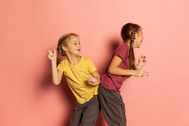 Portret van twee meisjes, kinderen, zussen dansen, plezier geïsoleerd over roze achtergrond