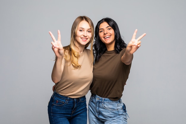 Portret van twee vriendinnen die twee vingers op een grijze muur laten zien en naar de voorkant kijken