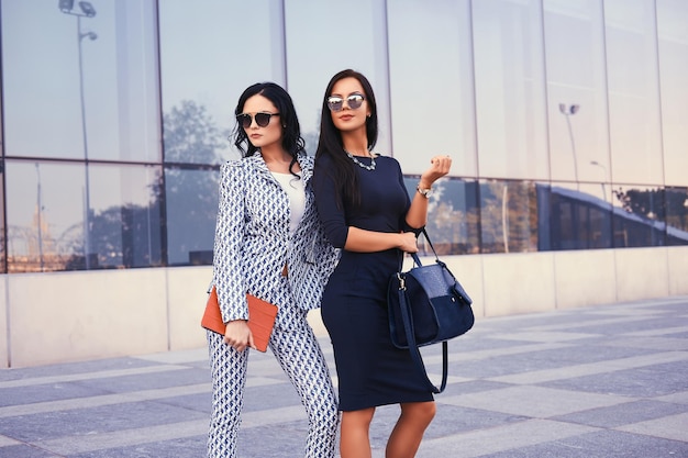 Portret van twee zakenvrouwen gekleed in stijlvolle formele kleding, staande in een centrum tegen een achtergrond van wolkenkrabber.