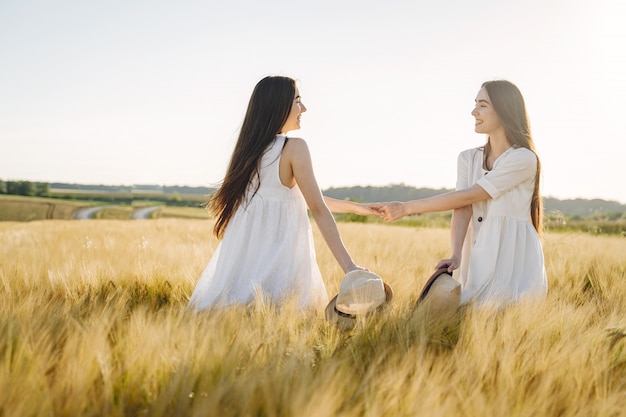 Portret van twee zussen in witte jurken met lang haar in een veld