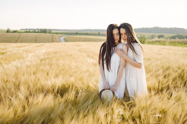 Portret van twee zussen in witte jurken met lang haar in een veld