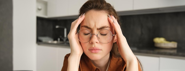 Gratis foto portret van vermoeide jonge werkende vrouw in bril houdt handen op het hoofd lijdt aan pijnlijke migraine heeft