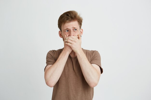 Portret van verrast bang bang jongeman op zoek in kant sluitende mond met handen.