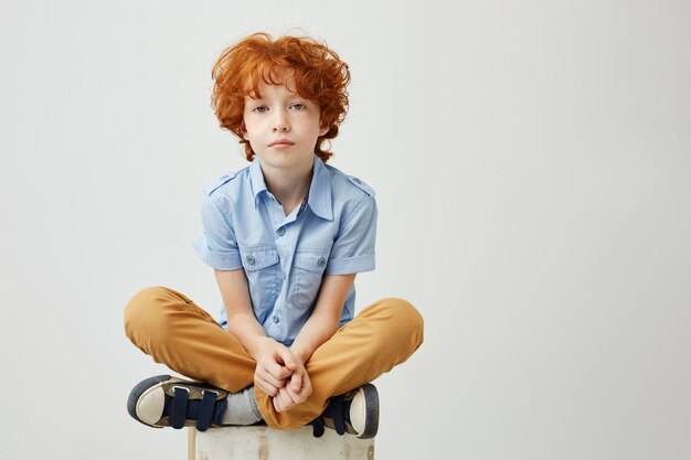 Portret van verveeld klein kind met rood haar en sproeten zittend op doos met ongelukkige uitdrukking